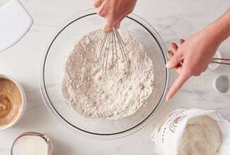 Baker whisking bowl of flour next to bag of medium rye flour