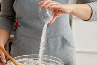 Hand pouring salt into bowl of dough