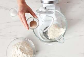 Baker adding yeast to the bowl of a stand mixer to make bread dough